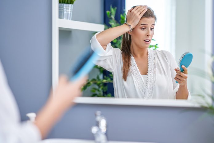 Happy woman brushing hair in bathroom having problem with hair loss