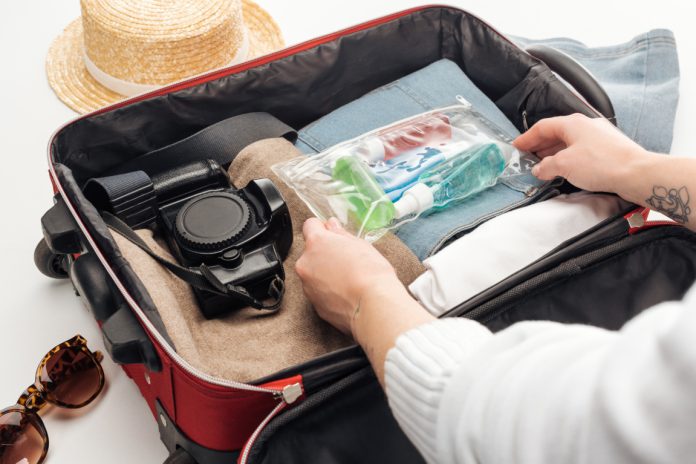 cropped view of woman packing travel bag with cosmetic bag with colorful bottles