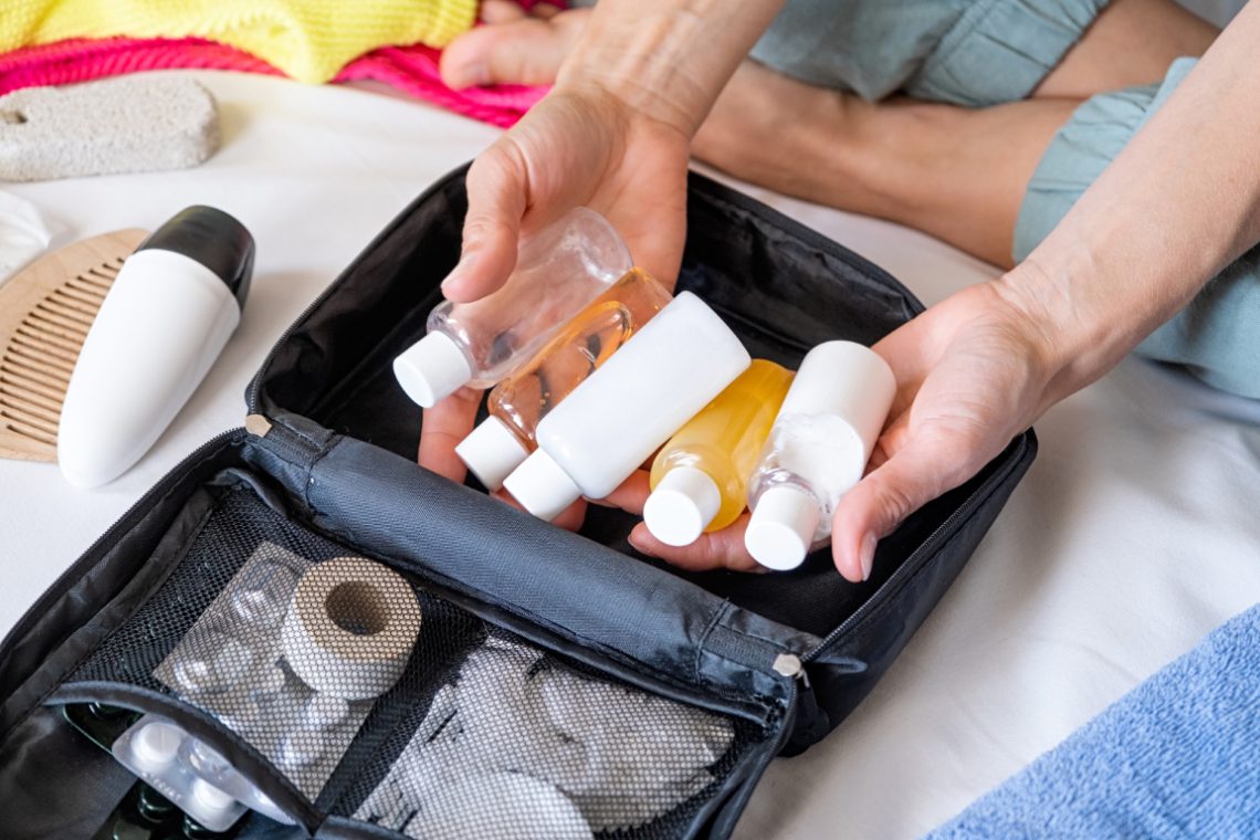 Woman hands holding travel cosmetics kit on bed , top view Woman hands holding travel cosmetics kit on bed , top view