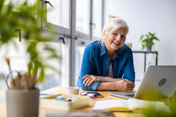 Portrait of smiling mature businesswoman sitting at desk with laptop in office