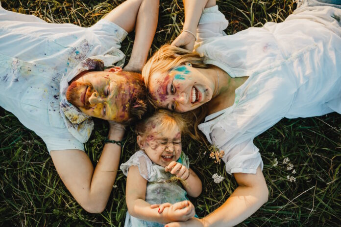 Mom, dad and their daughter covered with colorful paints lie on the green lawn Mom, dad and their daughter covered with colorful paints lie on the green lawn